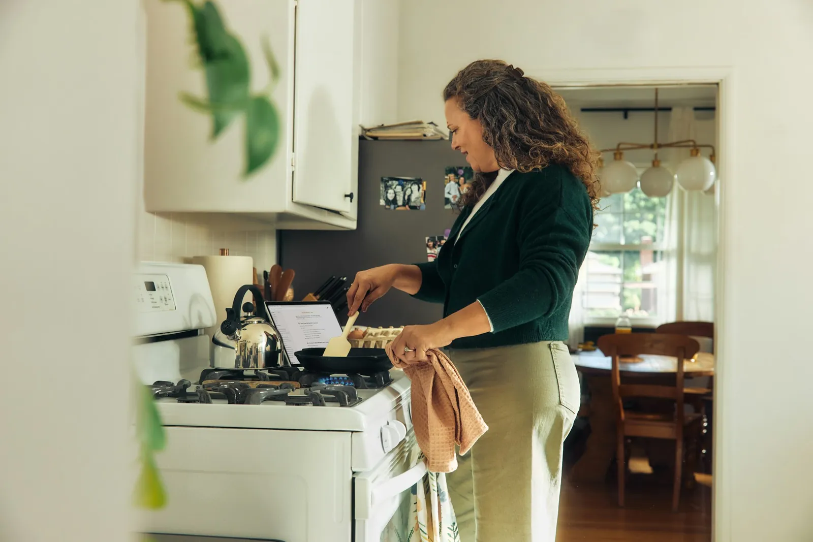 A woman cooking in a kitchen with a laptop nearby