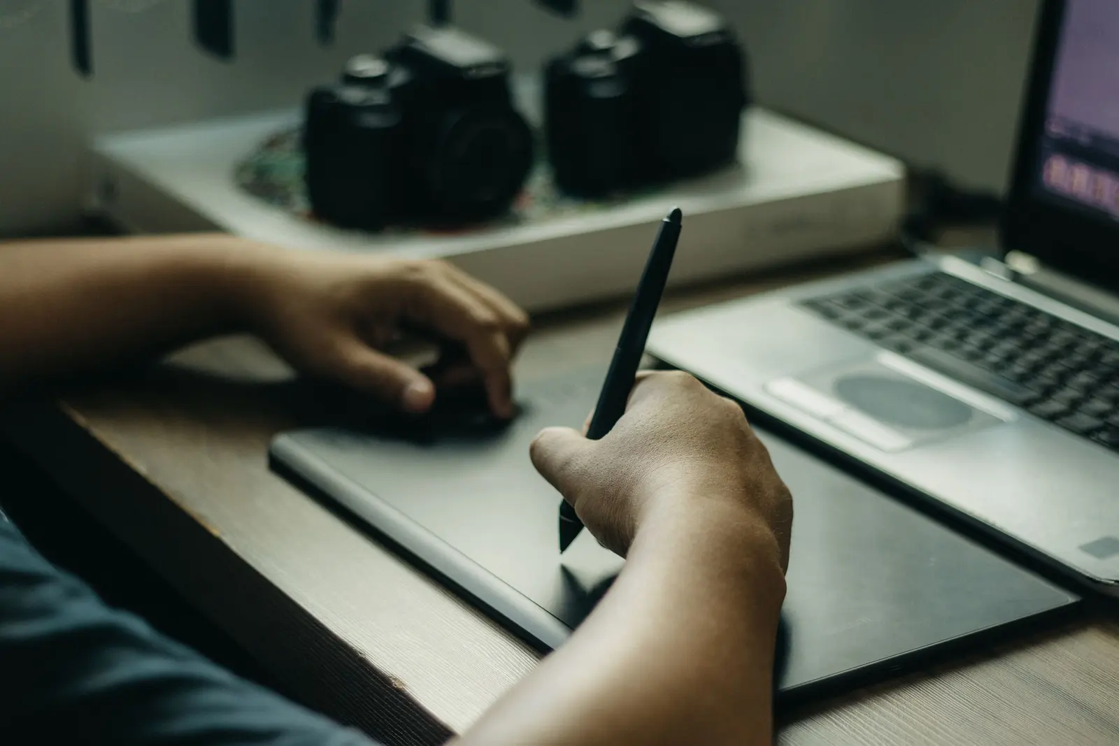 A person using a stylus and drawing tablet beside a laptop