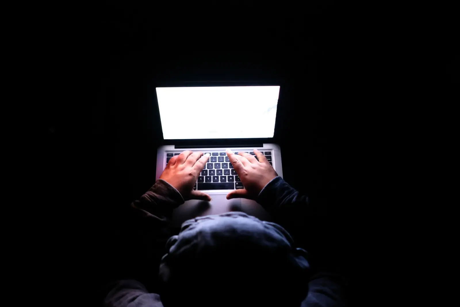 A person using a laptop in a dark room for a digital privacy task