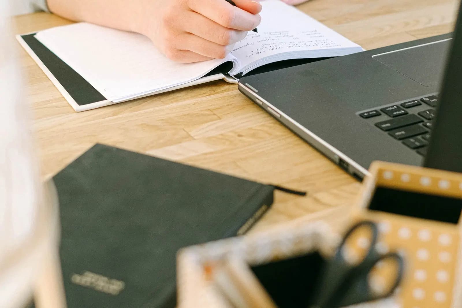 A person writing instructions in a notebook beside a laptop
